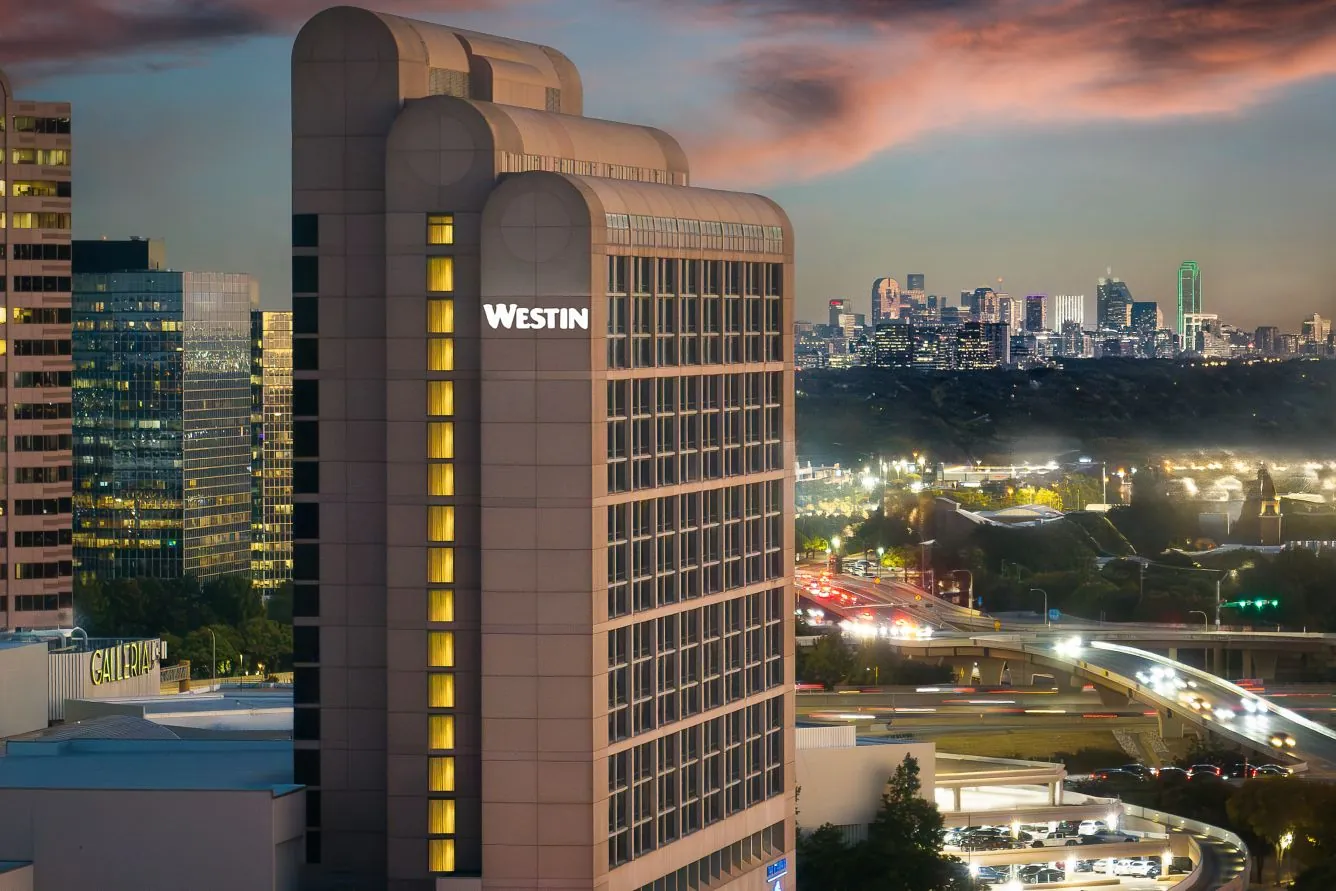 The Westin Galleria Dallas tower at dusk, with the Dallas skyline behind it